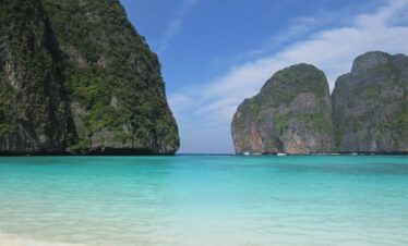 Tranquil tropical beach in Thailand featuring clear turquoise waters and lush cliffs.
