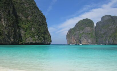 Tranquil tropical beach in Thailand featuring clear turquoise waters and lush cliffs.