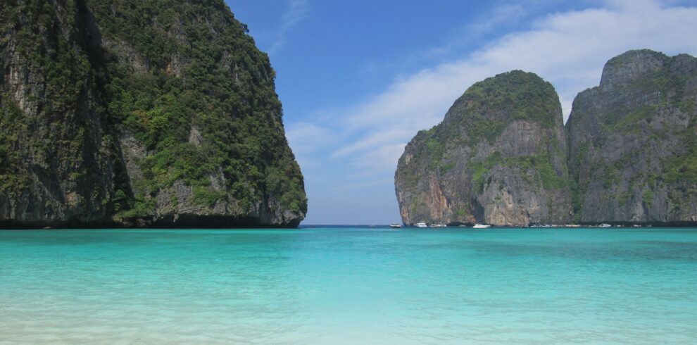 Tranquil tropical beach in Thailand featuring clear turquoise waters and lush cliffs.