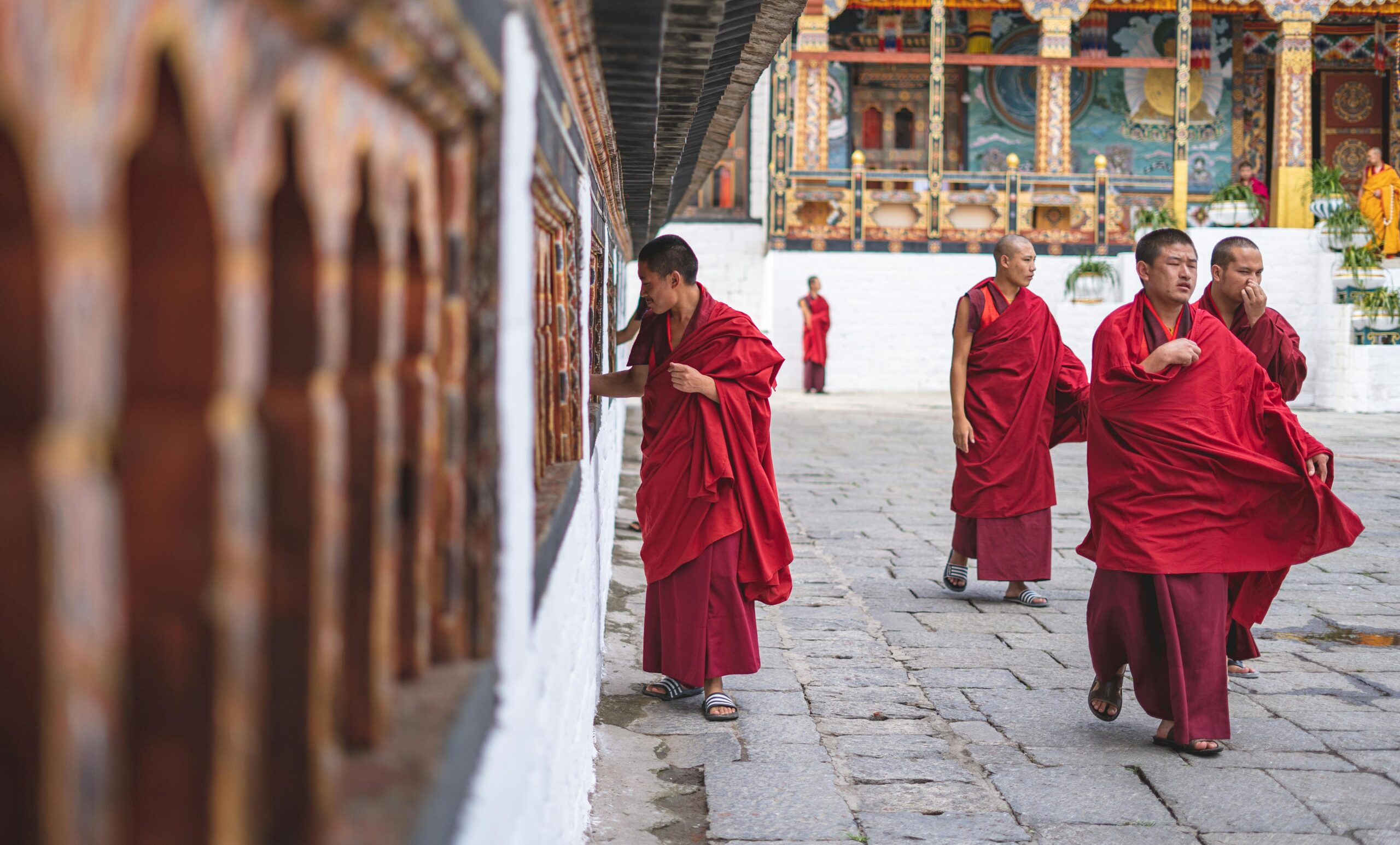 Buddhist monks in red robes walking and interacting in a Bhutan temple courtyard.
