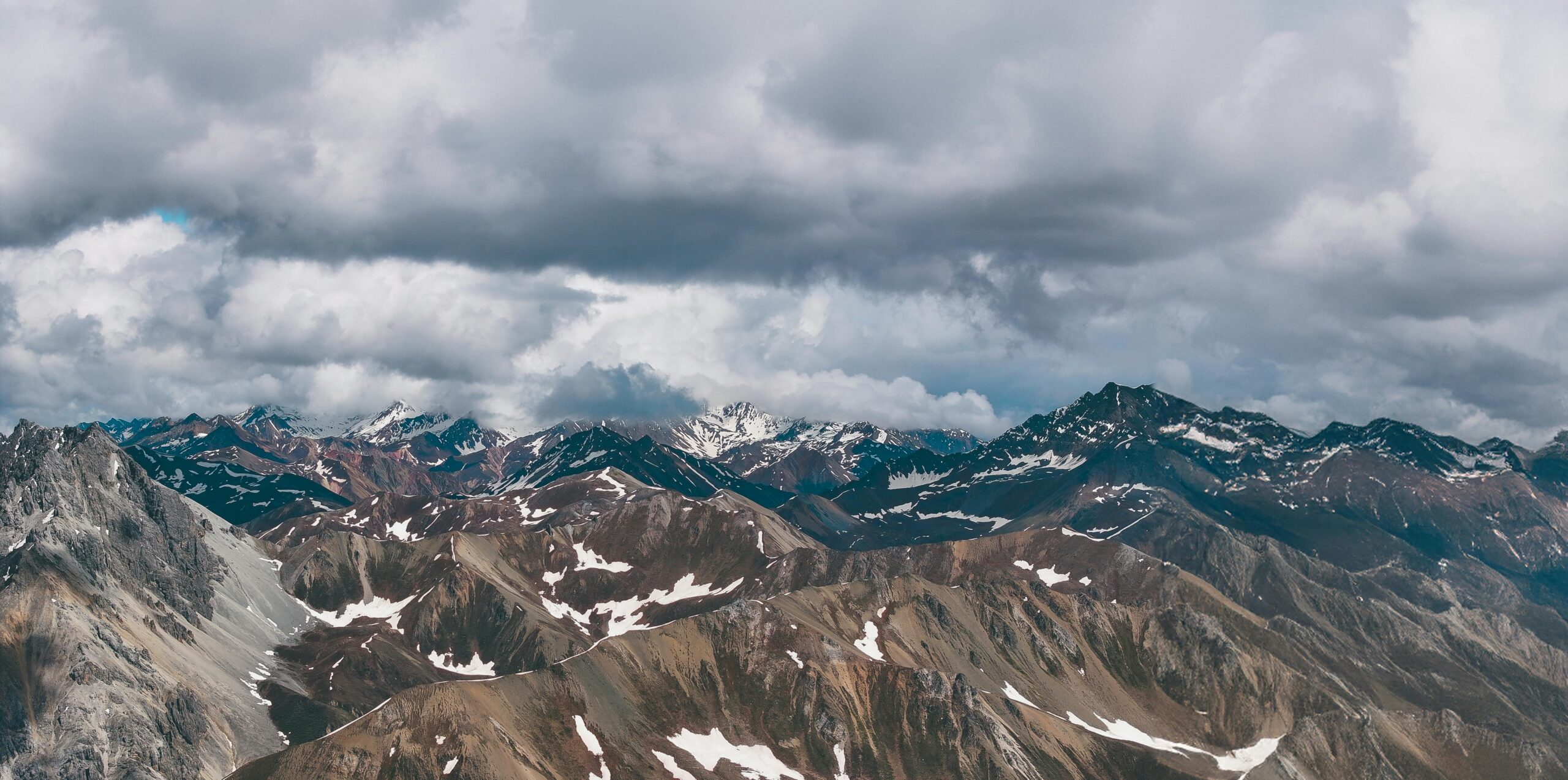 A breathtaking aerial view of the rugged, snow-capped Himalayan peaks under dramatic clouds.