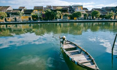 Peaceful scene of a traditional boat on the serene river in Hội An, Vietnam, showcasing historic architecture.