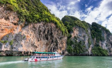 A boat cruise offers breathtaking views of lush cliffs under a bright blue sky.